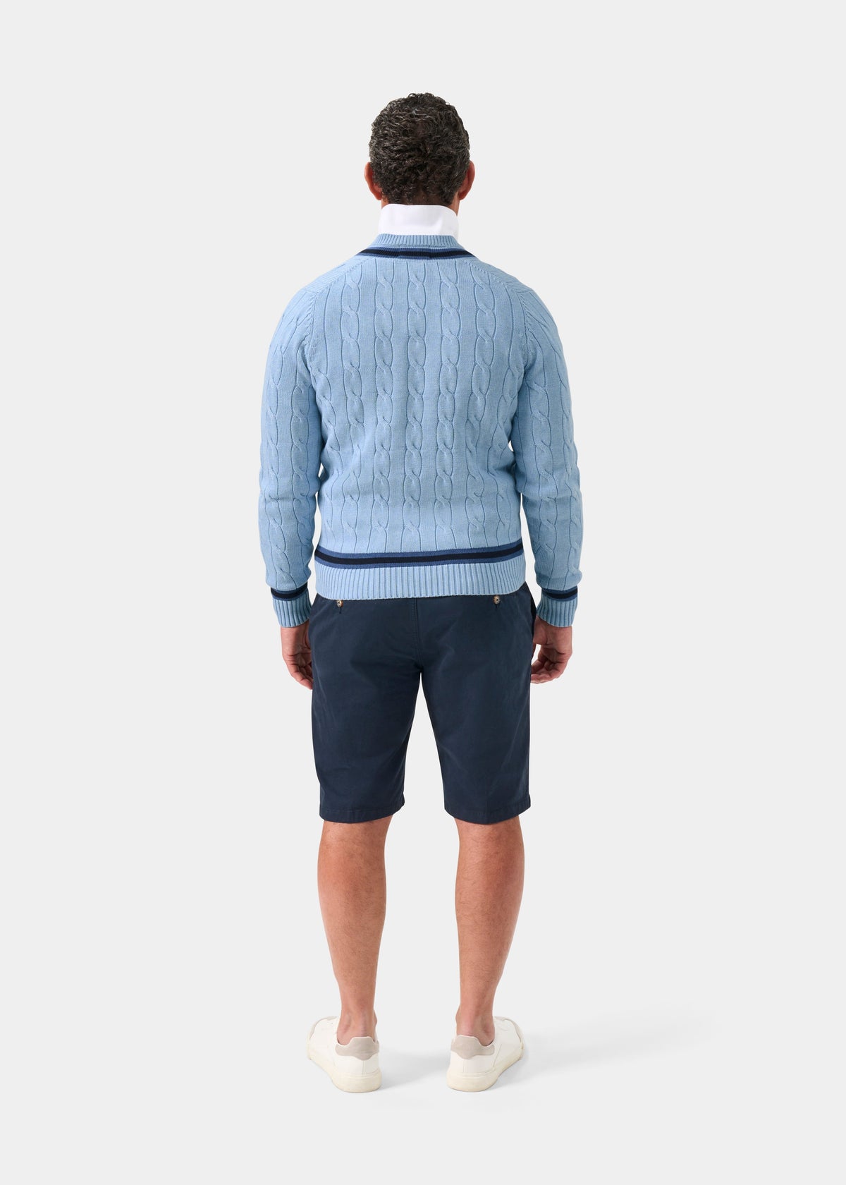 Steel blue cotton cable knit V-neck jumper with dark navy trim, back view, worn with navy shorts and white sneakers