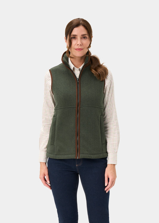 Woman in Aylsham Ladies Cedar Green fleece gilet, over plaid shirt and dark jeans, against a plain light background.