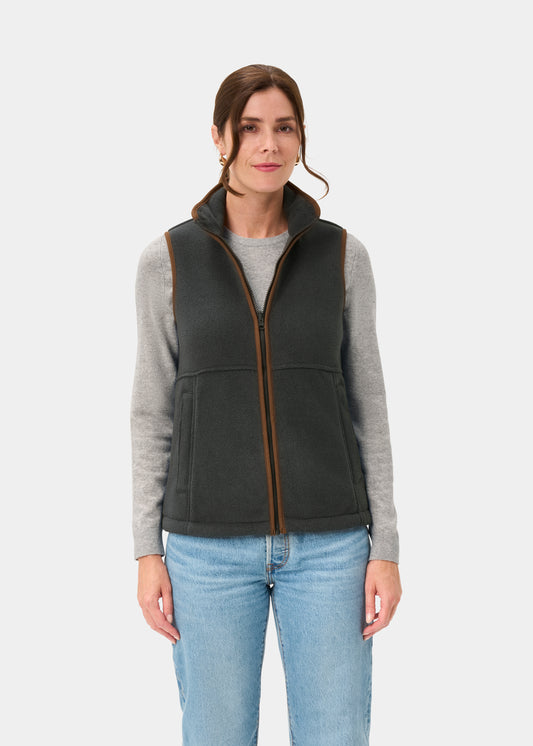 Woman in Aylsham Ladies Fleece Gilet in Gunmetal over gray long-sleeve shirt and blue jeans, on white background.