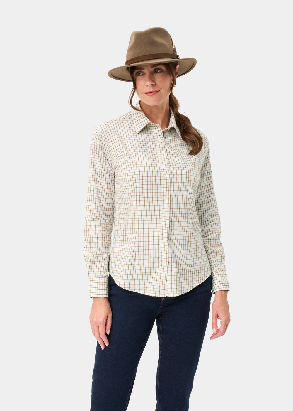 Woman in a Bromford Ladies Cotton Shirt in Olive Check, dark jeans, and brown hat stands against a white background.
