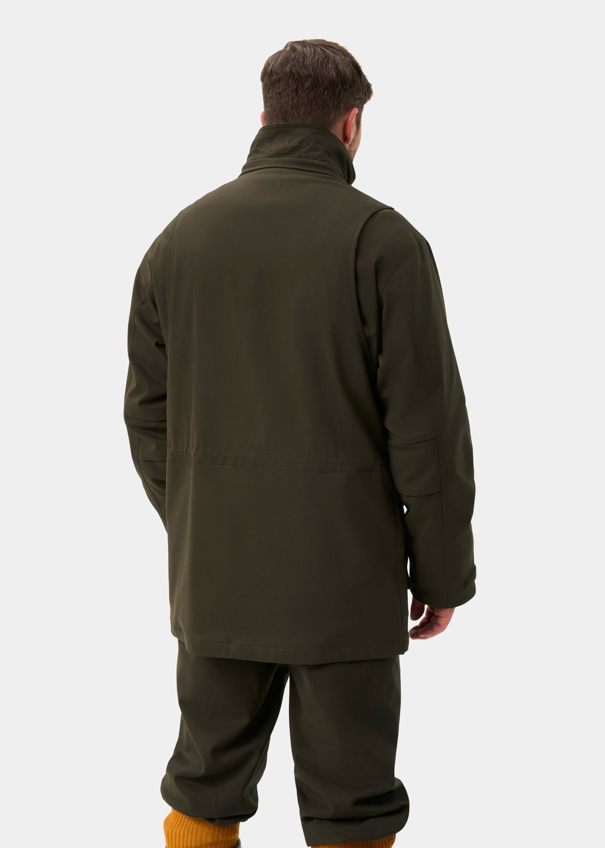 Man in Dunswell Men’s Waterproof Field Coat in Olive - Shooting Fit, back to camera, plain background.