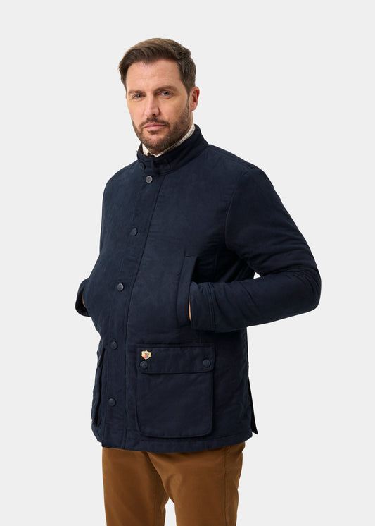 Man in Felwell Men’s Quilted Jacket in Dark Navy, hands in pockets, facing left on plain background.