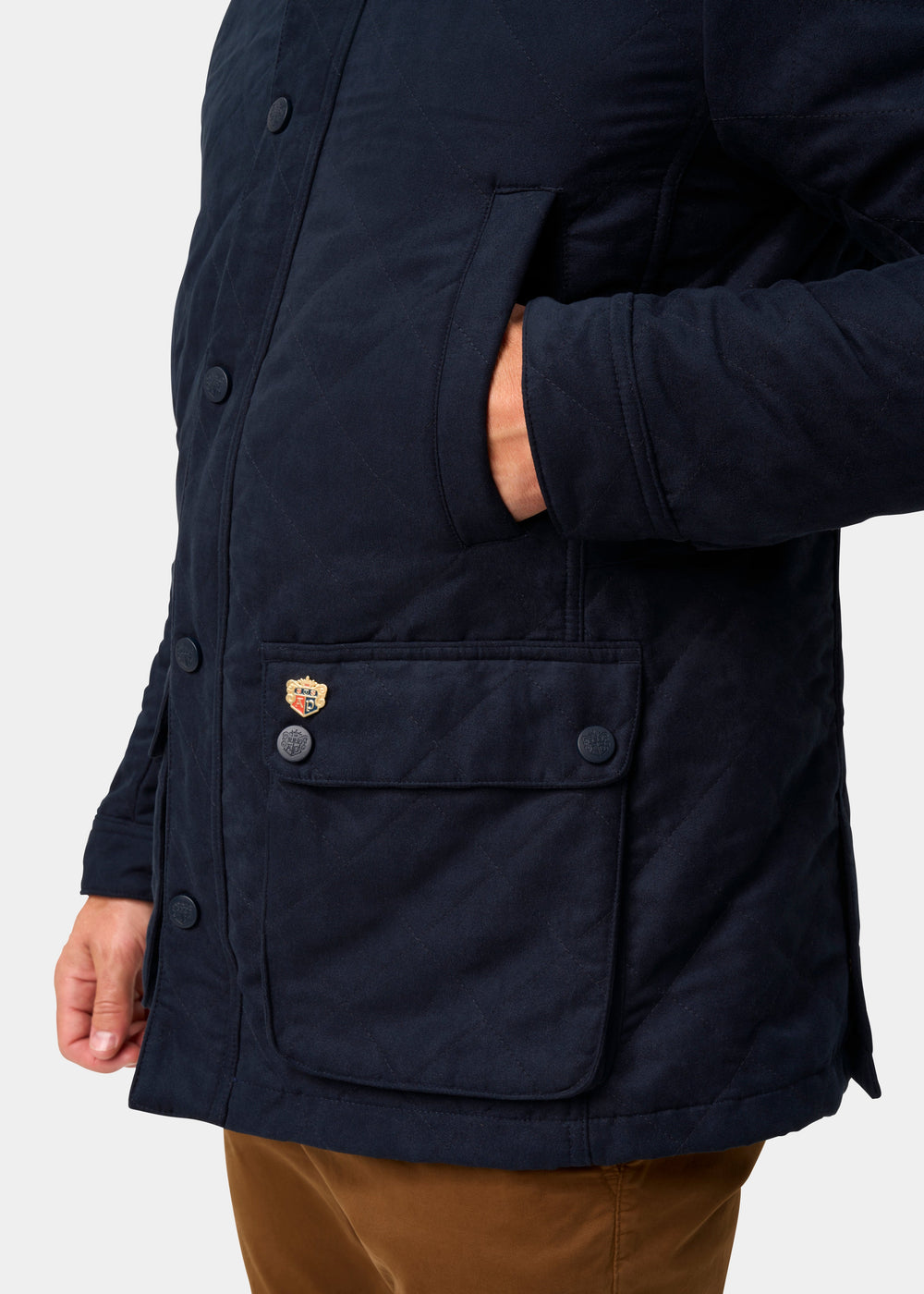 Man in Felwell Men’s Quilted Jacket in Dark Navy, hand in pocket; patch and buttons detail on front pocket.
