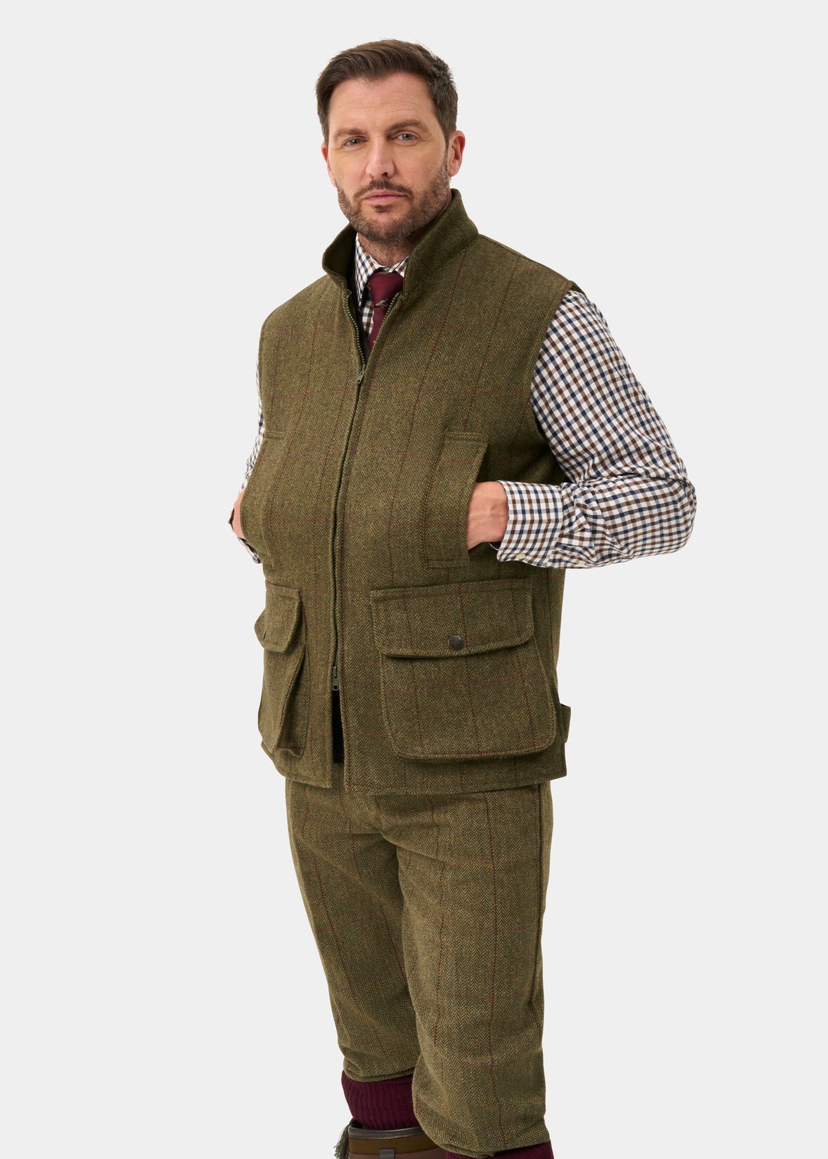 A man wearing the Rutland Men’s Tweed Water Repellent Waistcoat In Oakley over a plaid shirt and tie.