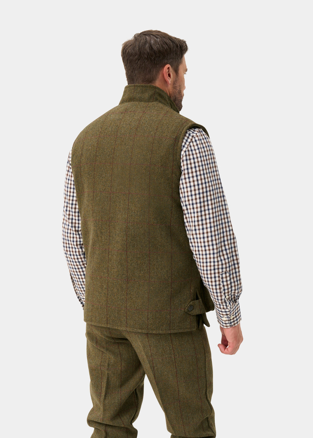 A man seen from behind wears an olive green Rutland Men’s Tweed Water Repellent Waistcoat In Oakley over a plaid shirt.
