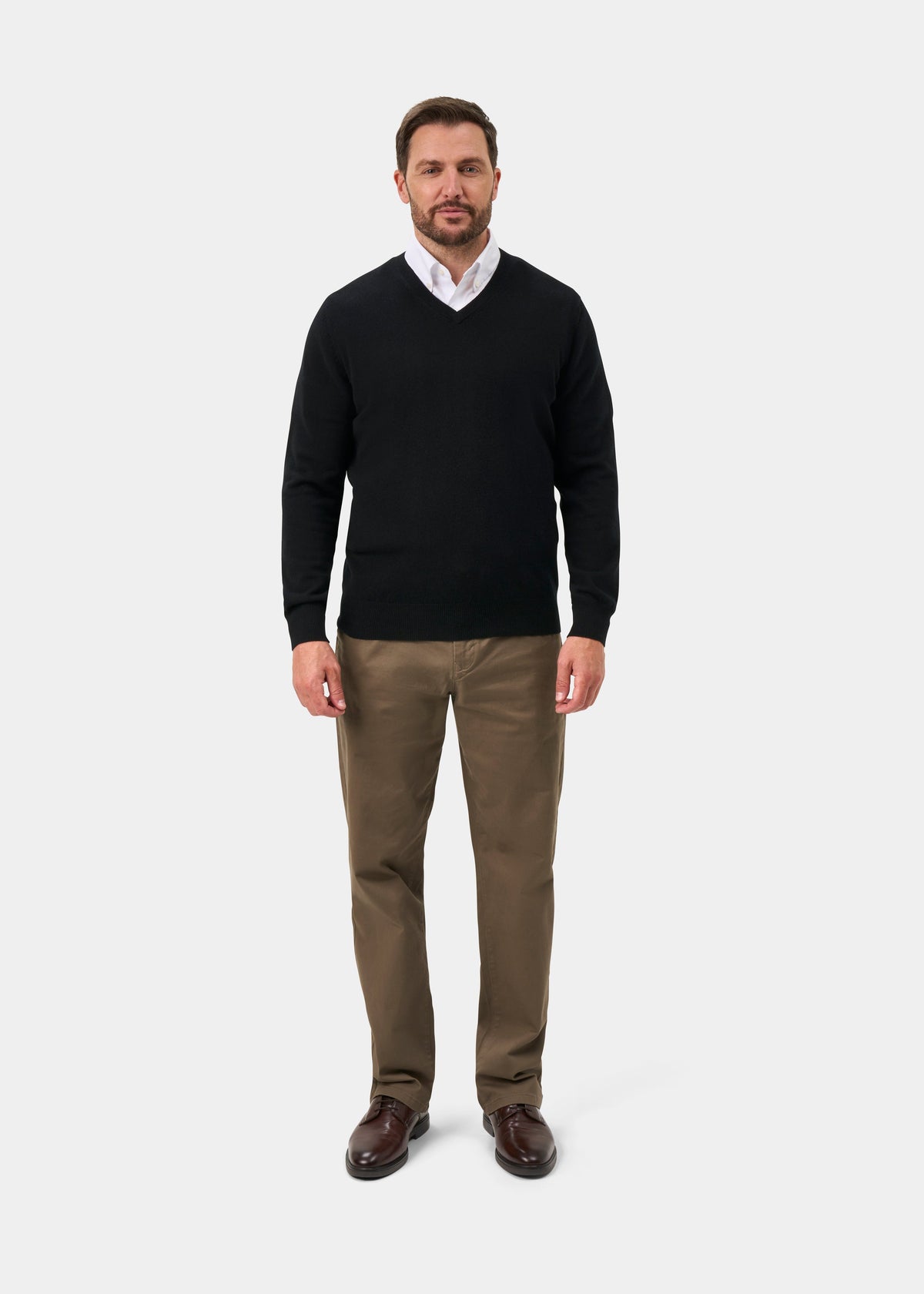 Man in Haddington Pure Cashmere V-Neck Jumper in Black, white shirt, khaki pants, brown shoes on plain background.