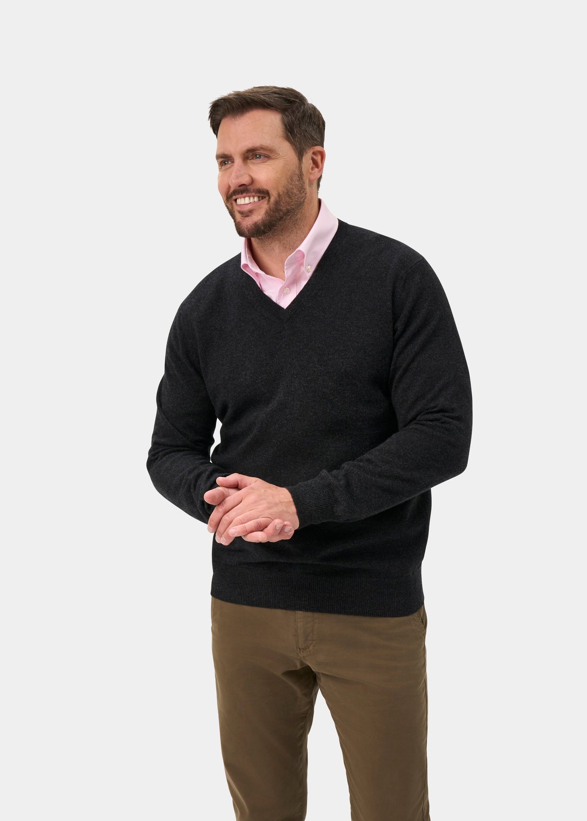 Smiling man in Haddington Pure Cashmere V-Neck Jumper in Charcoal with pink shirt and khaki pants on plain background.