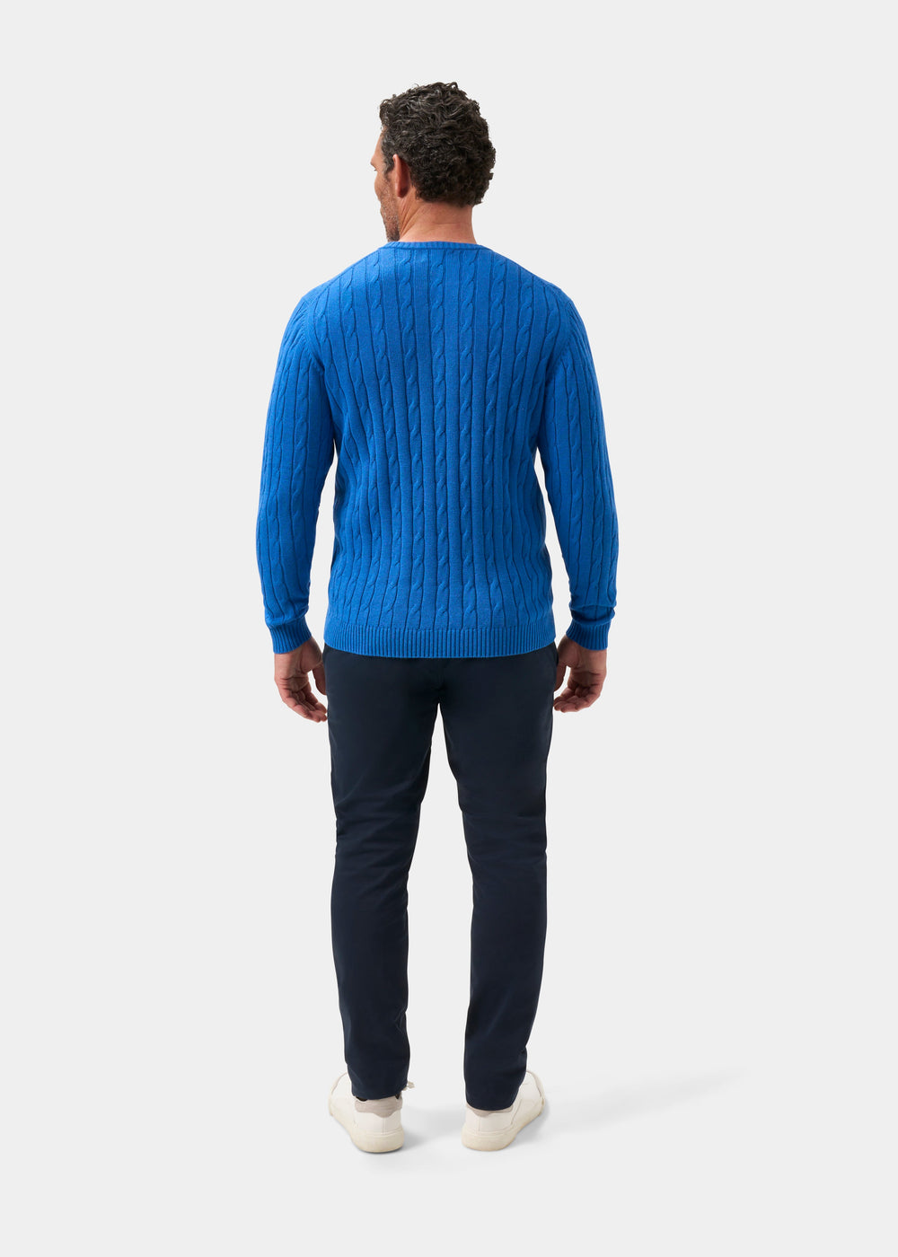 Man faces away, wearing Honley Cotton Cashmere Cable Knit Crew Neck Jumper in Regatta with dark pants on white background.