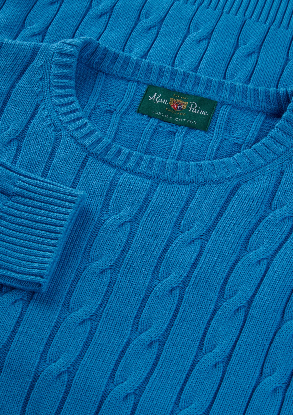 Close-up of Honley blue lagoon cable crew neck jumper; visible collar tag: Alan Paine Luxury Cotton Cashmere.