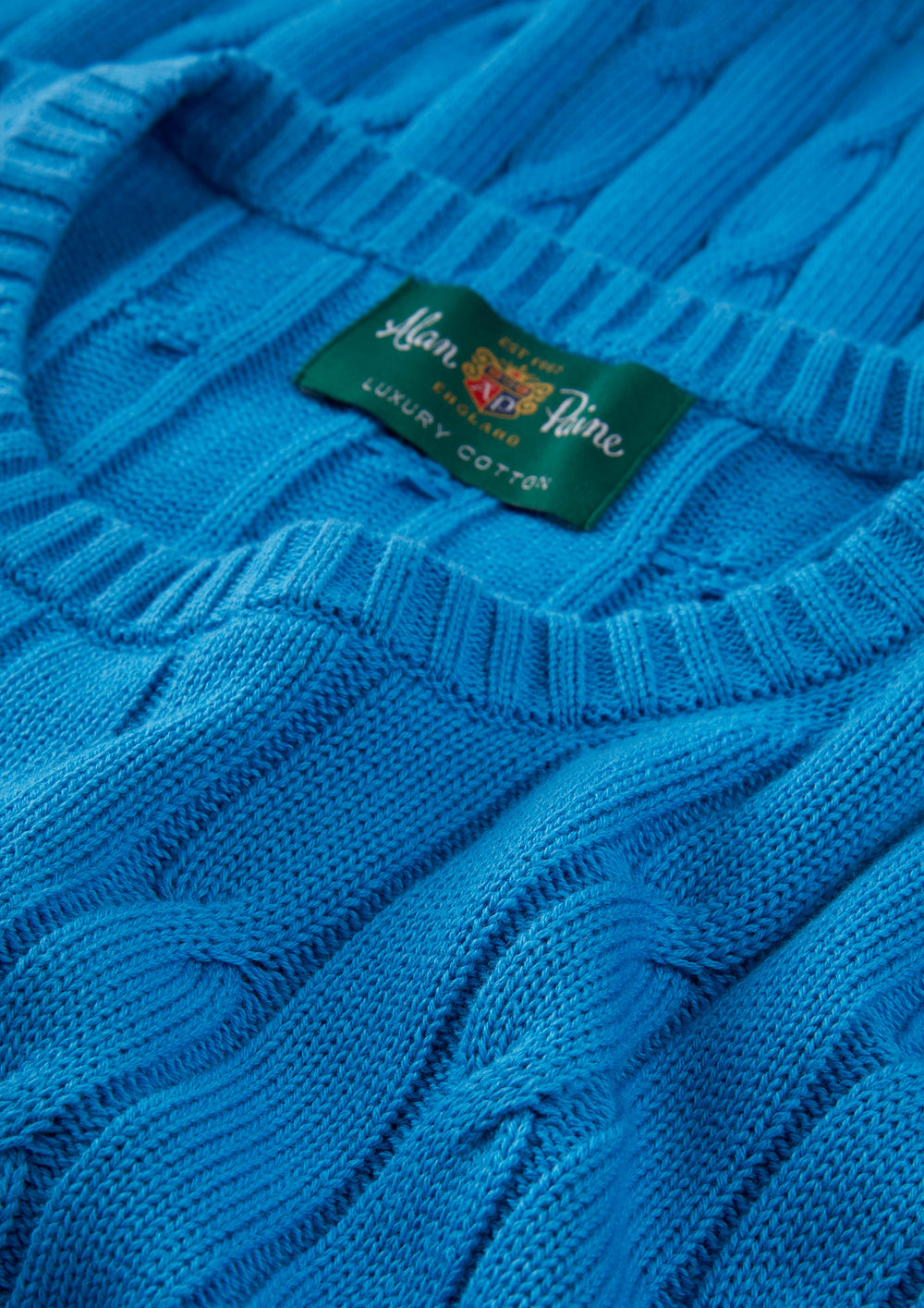 Close-up of Honley Cotton Cashmere Cable Knit Crew Neck Jumper in Blue Lagoon with visible green Alan Paine label.