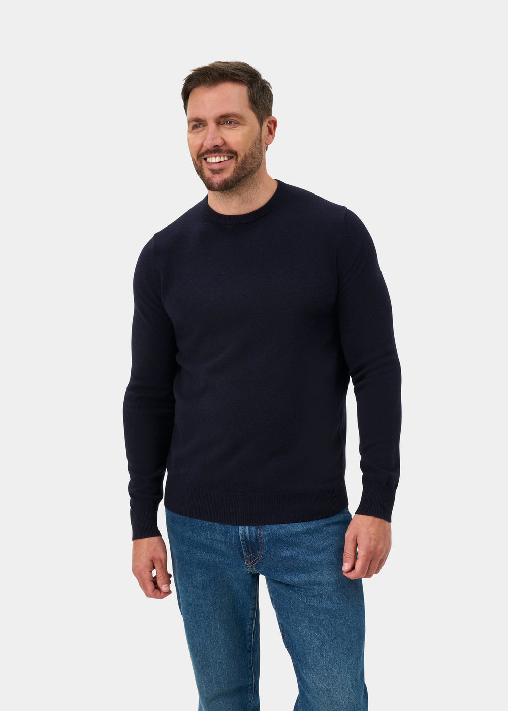 Man in a Brisbane Geelong Wool Crew Neck Jumper in Dark Navy and blue jeans smiles against a white background.