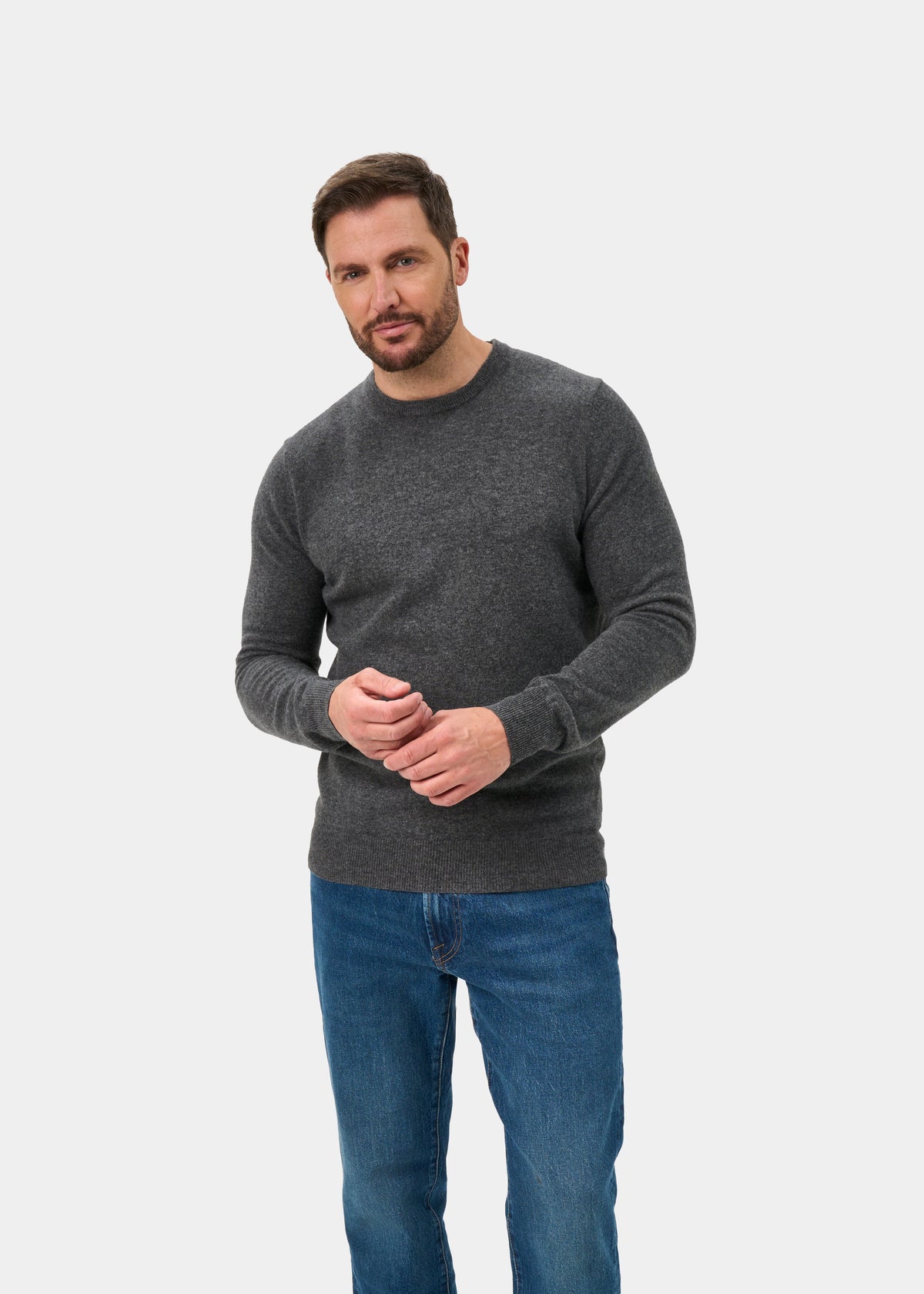 Man wears Brisbane Geelong Wool Crew Neck Jumper in Derby, regular fit, with blue jeans against a white background.