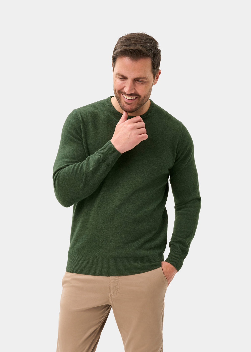 Man smiles in a rosemary Brisbane Geelong Wool Crew Neck Jumper and beige pants, hand on chin, other in pocket.