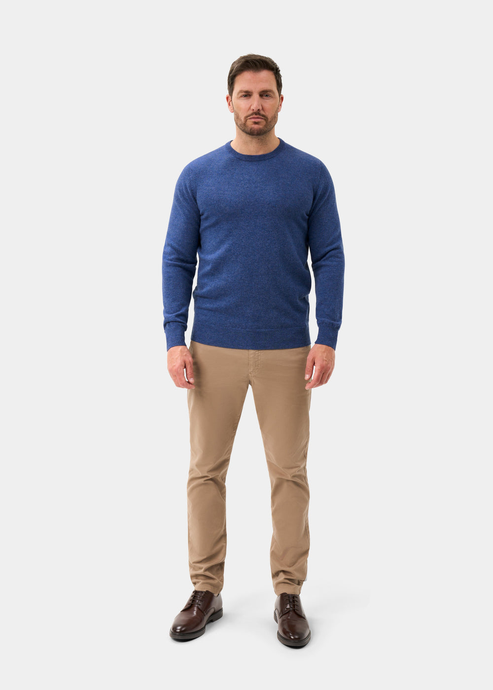 Man in blue Brisbane Geelong Wool Crew Neck Jumper, khaki pants, and brown shoes stands facing forward on white.