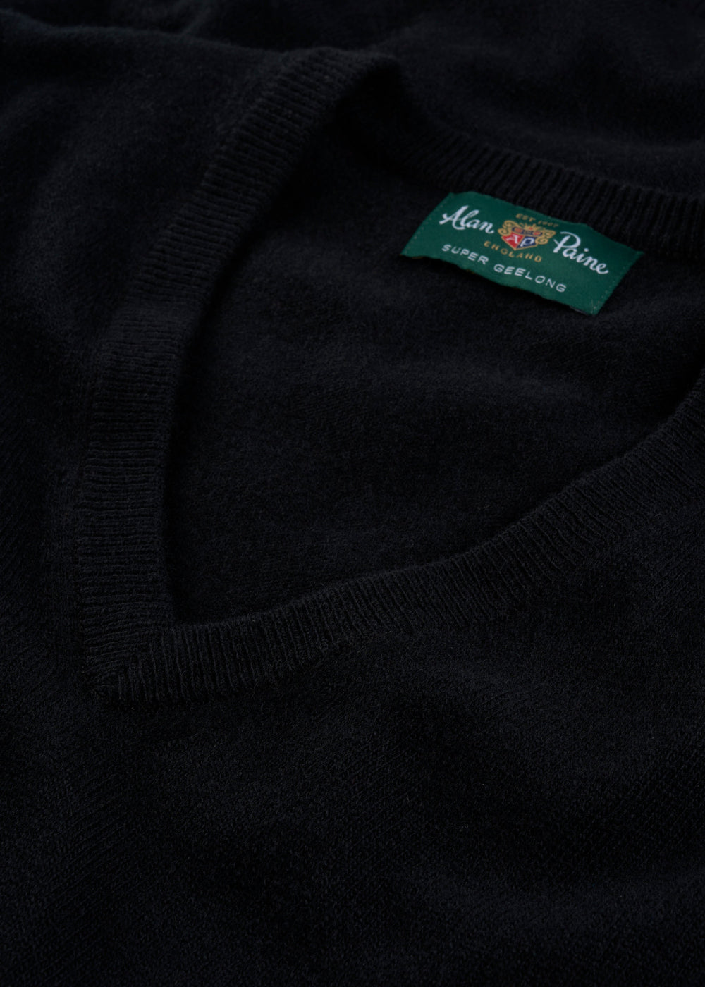 Close-up of the Albury Geelong Wool V-Neck Jumper in black, regular fit, featuring its branded label.