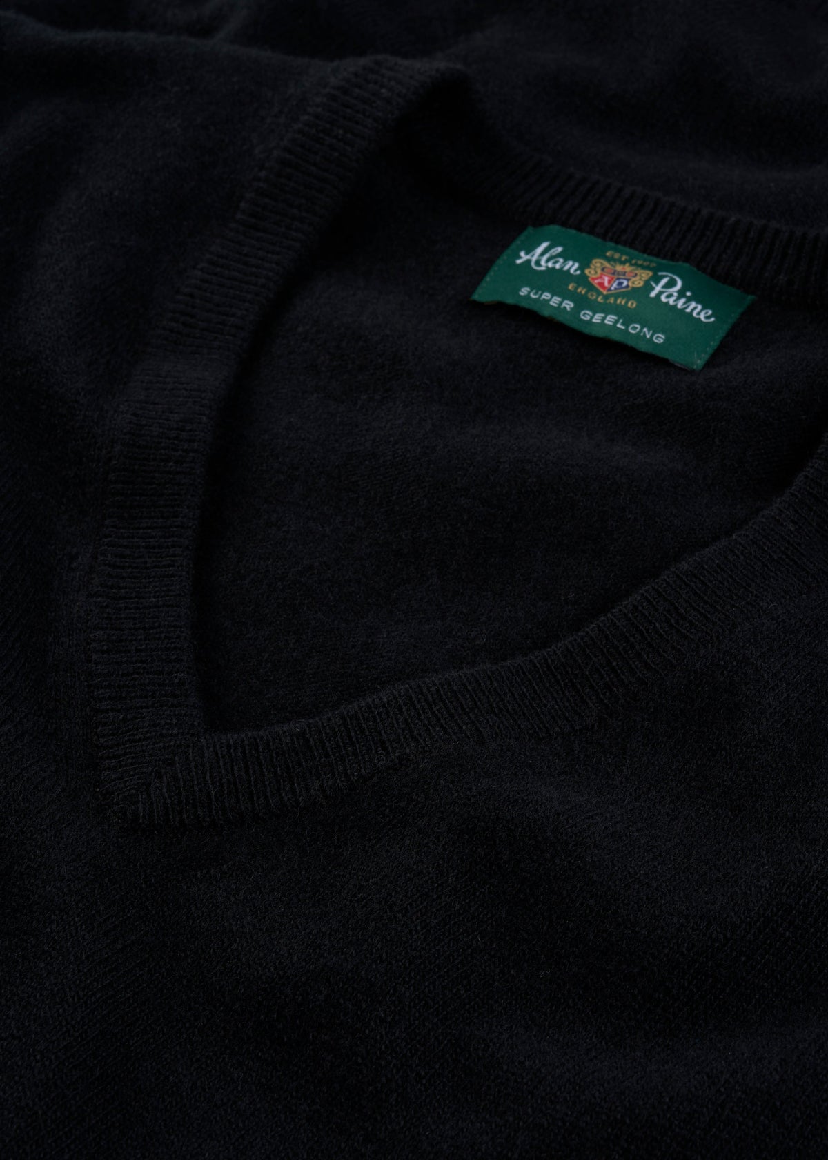 Close-up of the Albury Geelong Wool V-Neck Jumper in black, regular fit, featuring its branded label.
