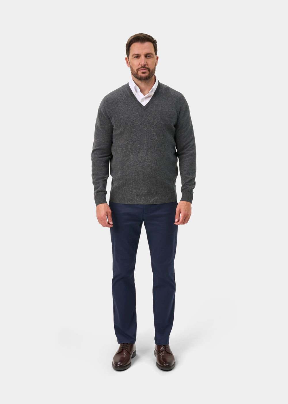 Man wearing Albury Geelong Wool V-Neck Jumper in Derby, white shirt, navy pants, and brown shoes.