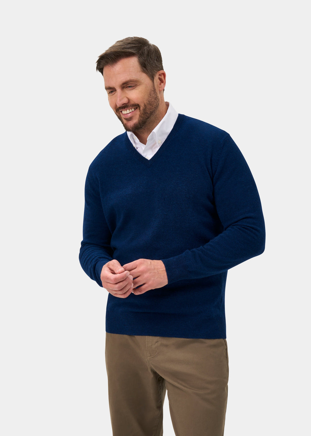 Man in an Albury Geelong Wool V-Neck Jumper in Indigo, over a white shirt and khakis, smiling hands clasped.
