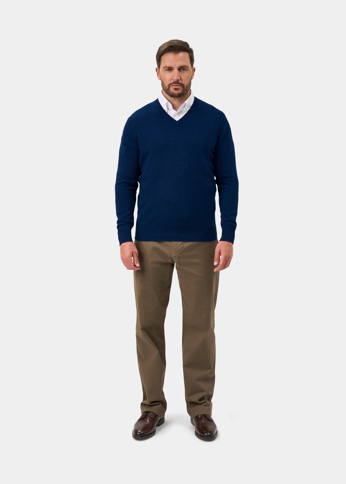 Man in an Albury Geelong Wool V-Neck Jumper in indigo, white shirt, khaki pants, and brown shoes on white background.