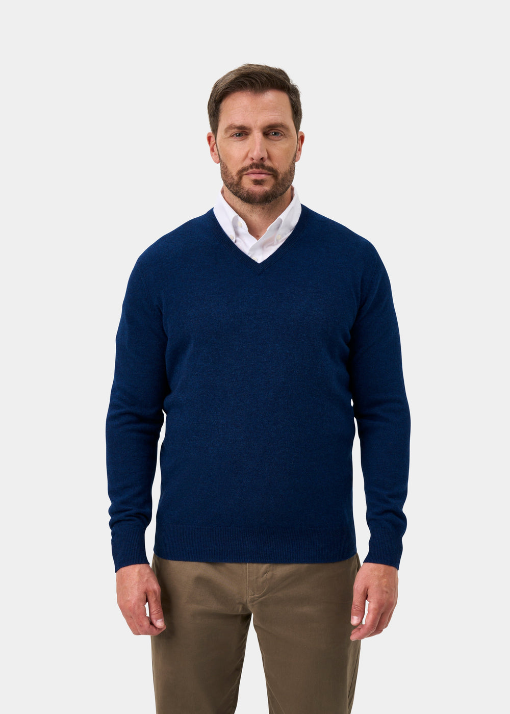 Man wears Albury Geelong Wool V-Neck Jumper in Indigo over a white shirt and khaki pants, against a light background.