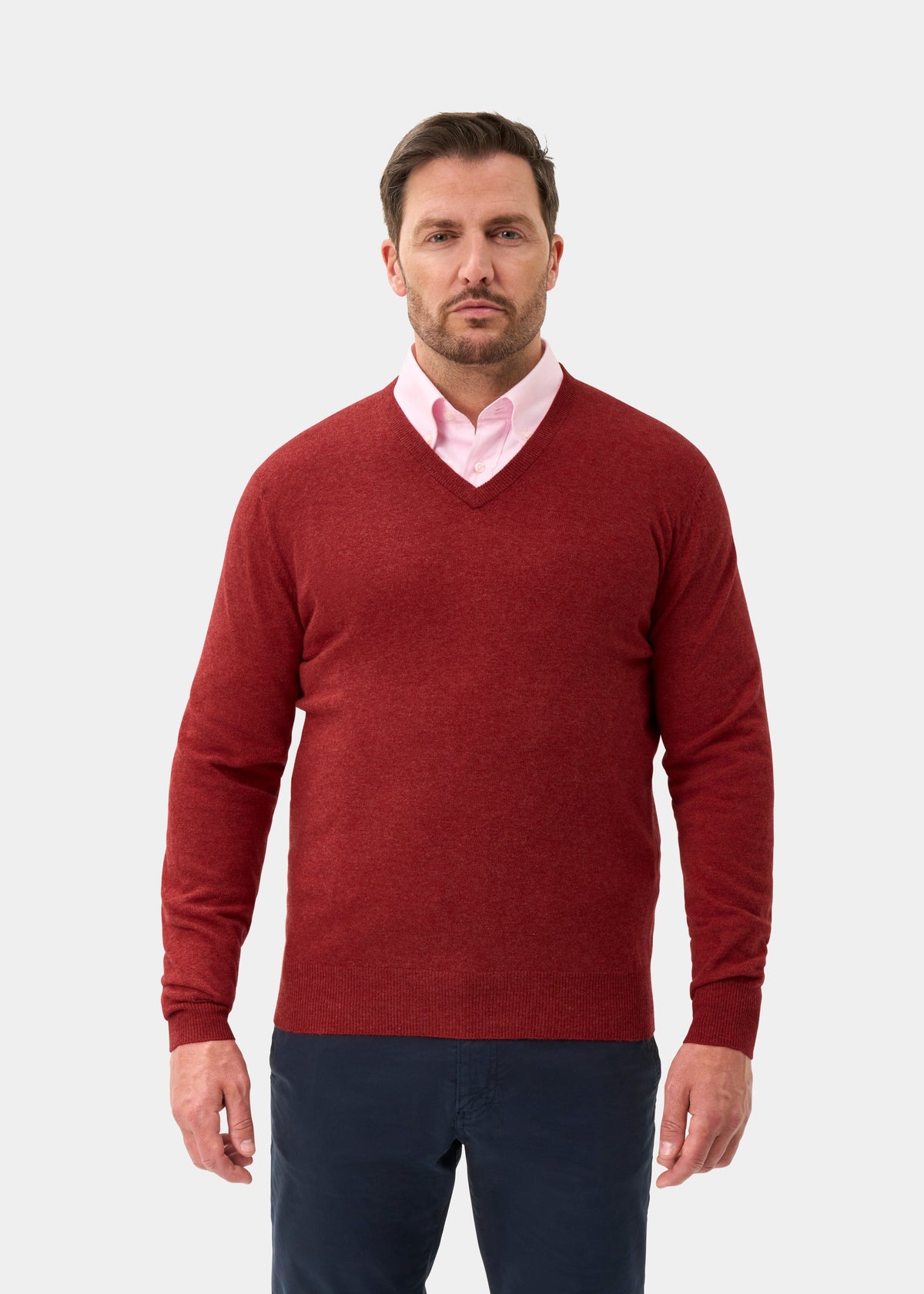 Man in Albury Geelong Wool V-Neck Jumper in Poppy Melange over pink shirt, standing against plain white background.
