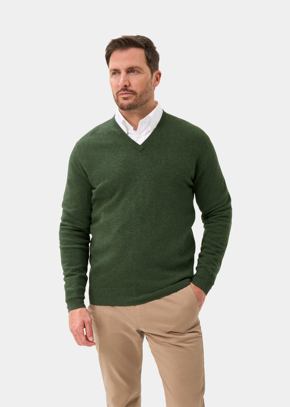 Man in Albury Geelong Rosemary V-Neck Jumper over white shirt, tan pants, standing with one hand in pocket.