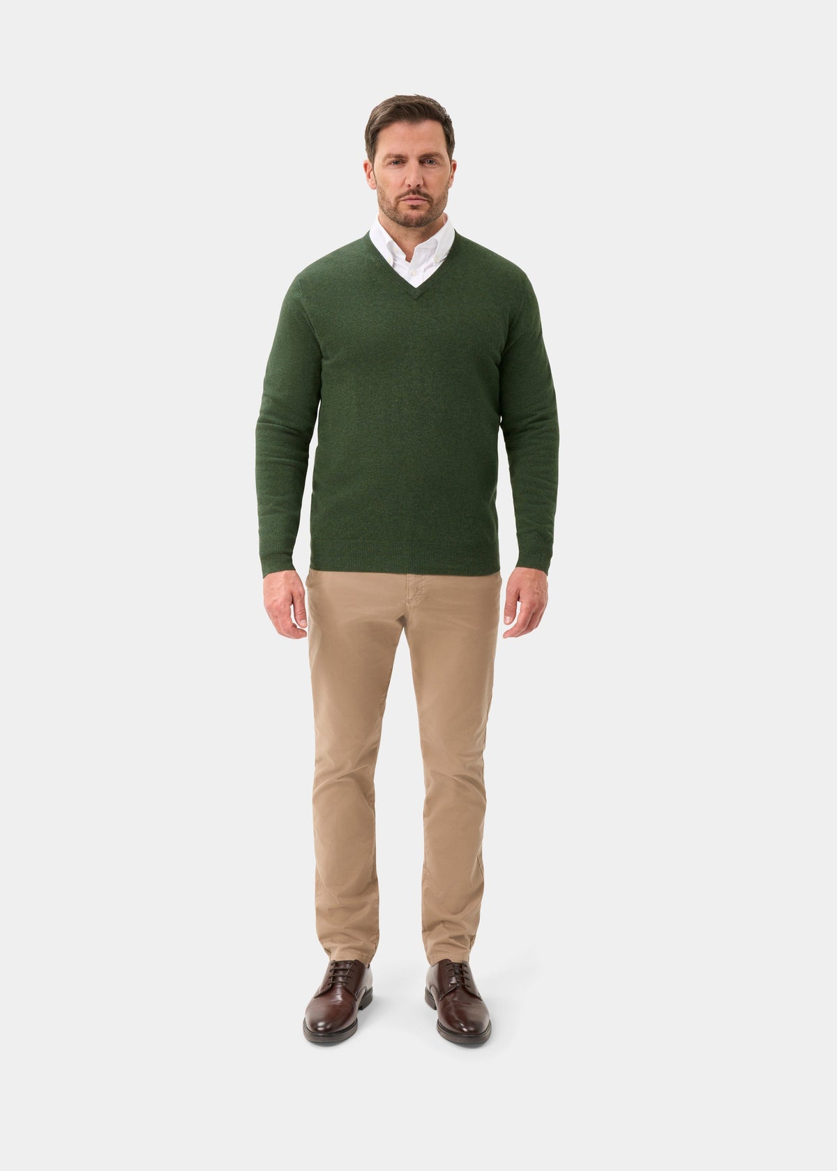 Man wears Albury Geelong Wool V-Neck Jumper in Rosemary, white shirt, khaki pants, and brown shoes on white background.