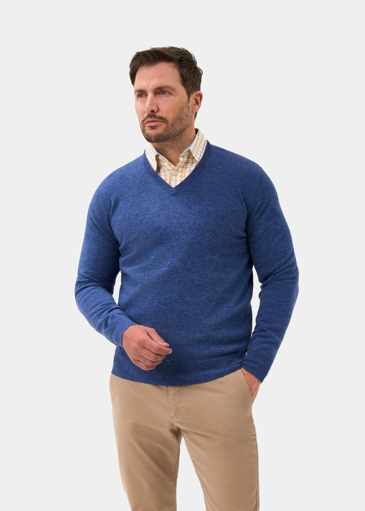 Man in Albury Geelong Wool V-Neck Jumper in Ullswater, beige pants, hand in pocket against plain background.