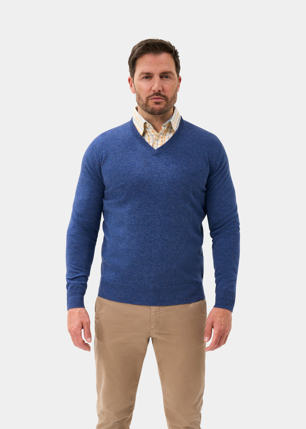 Man in an Albury Geelong Wool V-Neck Jumper in Ullswater and khaki pants stands against a plain white background.