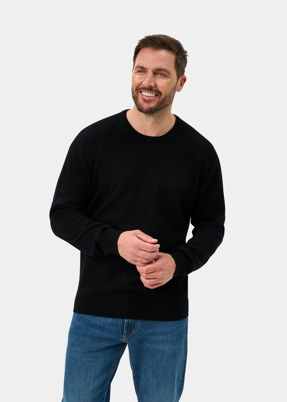 Man in Dorset Lambswool Crew Neck Jumper in Black, classic fit, with blue jeans against a plain background.