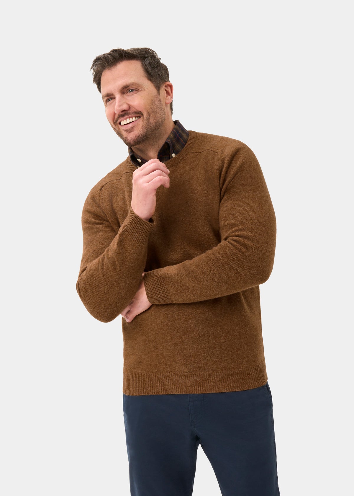 Man in Dorset Lambswool Crew Neck Jumper In Driftwood, classic fit, smiles against a plain light background.