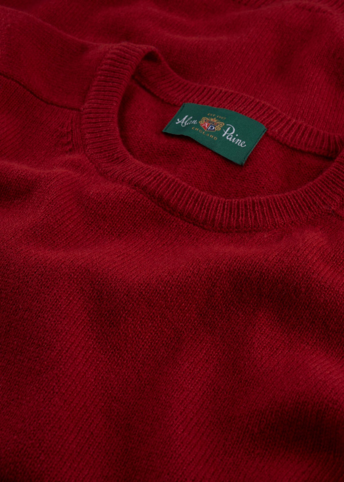 A close-up of the Lenzie Lambswool Crew Neck Jumper in Dubonnet, featuring a green Alan Paine label.