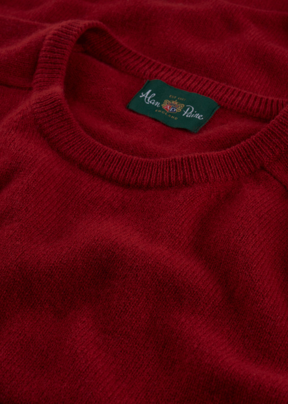 Close-up of Dorset Lambswool Crew Neck Jumper in Dubonnet with green Alan Paine label on the collar.
