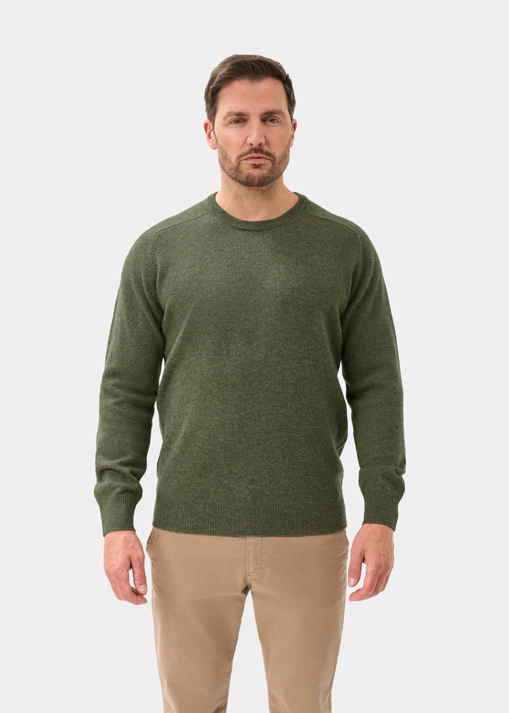 Man in Dorset Lambswool Crew Neck Jumper in Landscape, classic fit, with beige pants stands against white background.