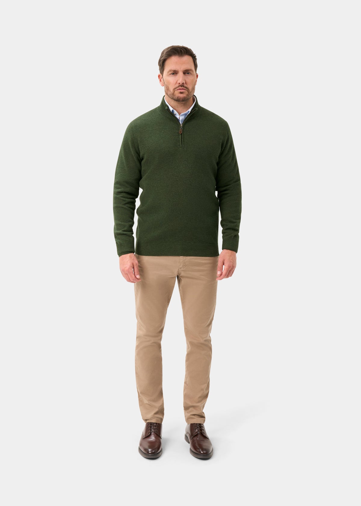 A man wearing a Sutherland Lambswool Quarter Zip Jumper In Rosemary, light blue shirt, tan trousers, and brown shoes.