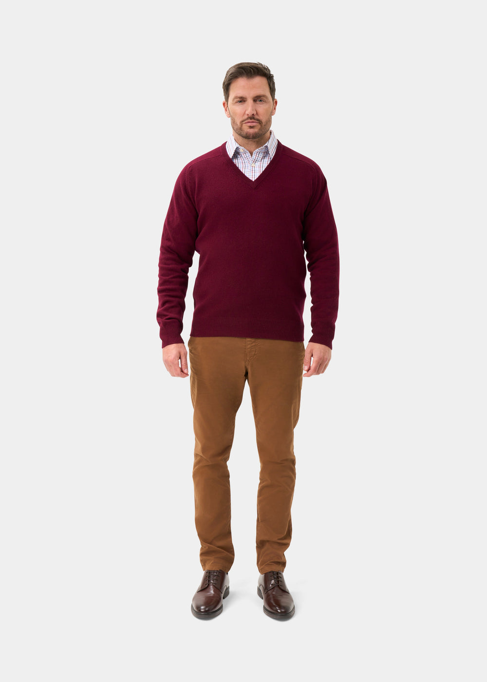 Man wearing Hampshire Lambswool V-Neck Jumper in Bordeaux, collared shirt, brown pants, and shoes on white background.