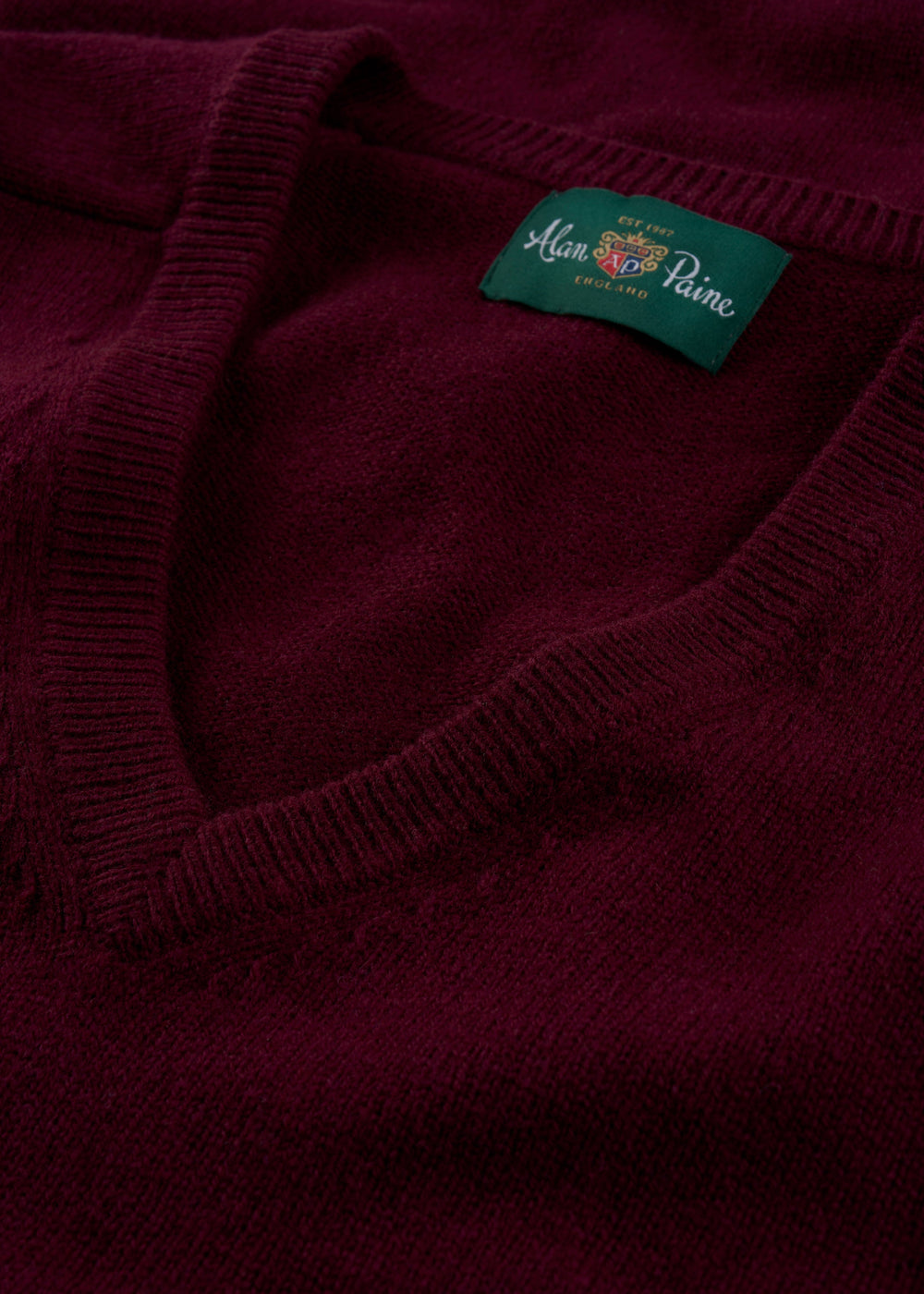Close-up of the Hampshire Lambswool V-Neck Jumper in Bordeaux, classic fit, with a green Alan Paine England label.