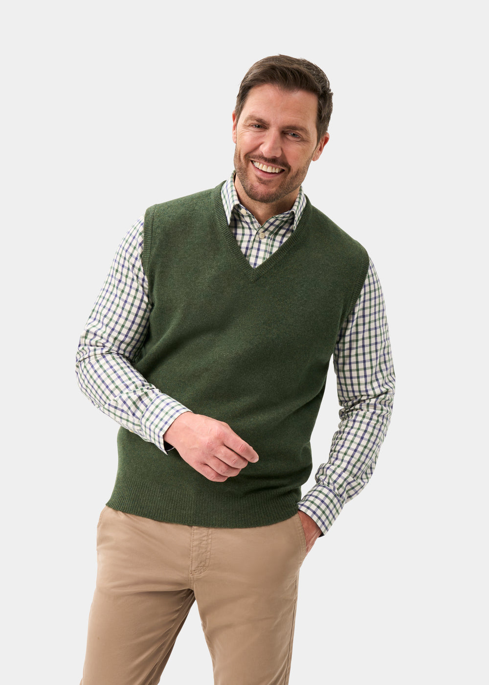 A smiling man wears a Norfolk Lambswool V-Neck Slipover In Rosemary over a plaid button-down shirt and tan trousers.