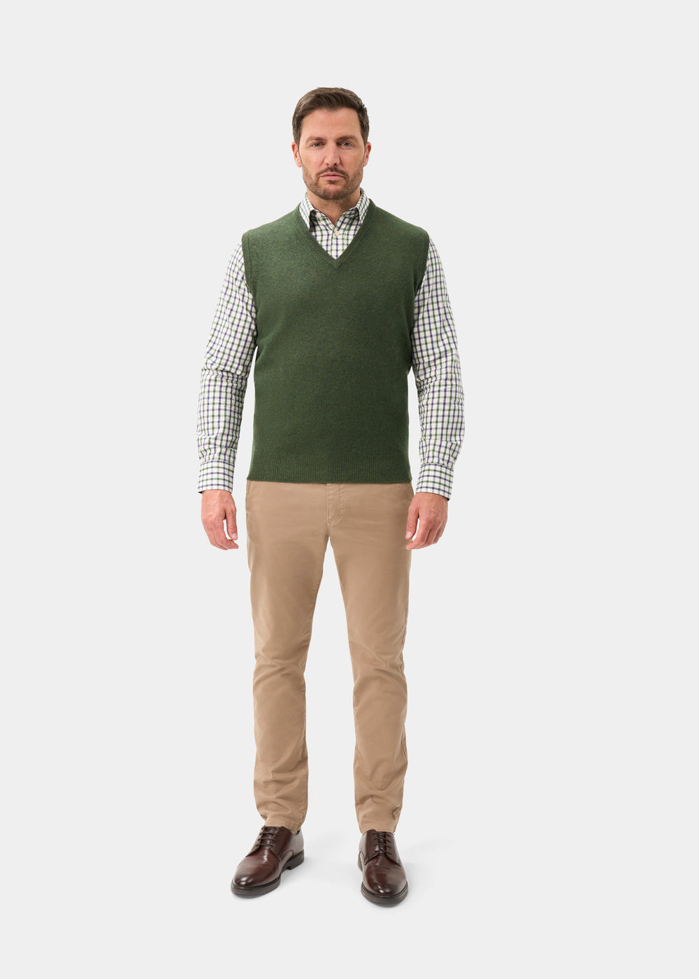 Man wearing a rosemary Norfolk Lambswool V-Neck Slipover over a plaid shirt, khaki trousers, and brown leather shoes.