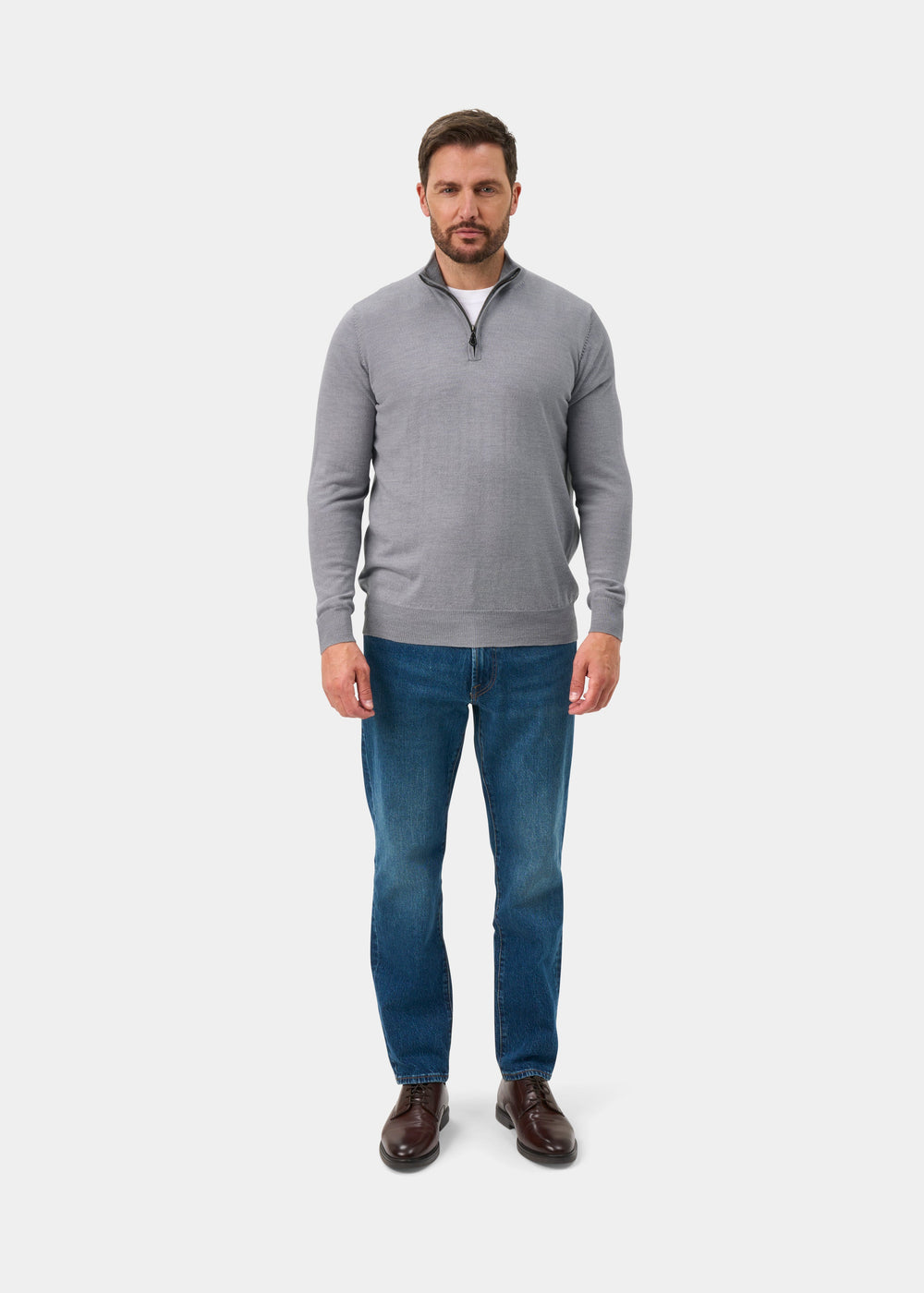 Man wears Barton Merino Wool Quarter Zip Jumper in Light Grey Mix, blue jeans, and brown shoes on white background.