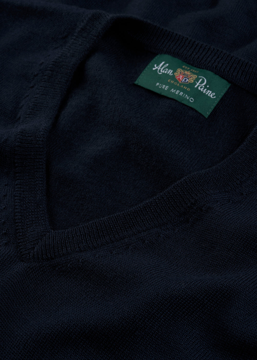 Close-up of a dark navy knit sweater with a green neck label reading 'Aman of Paine Pure Merino'.