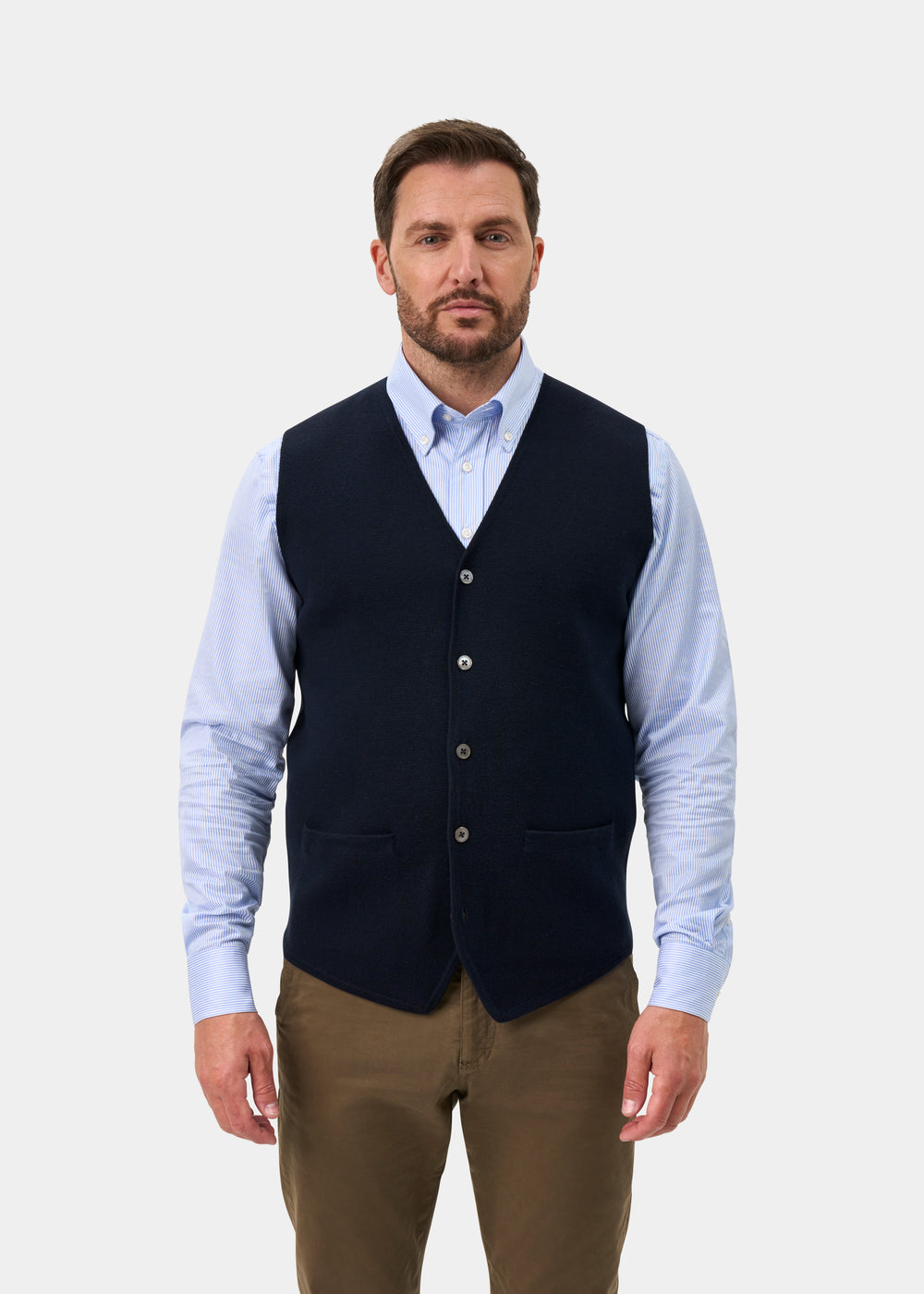 Man wearing a Thornley Merino Wool Tailored Dark Navy Waistcoat over a light blue striped dress shirt and brown trousers.