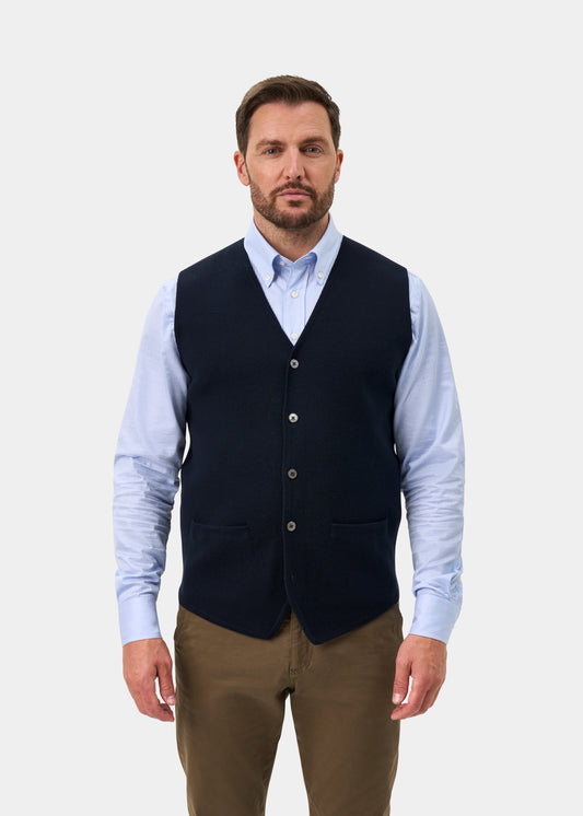 Man wearing a Thornley Merino Wool Tailored Dark Navy Waistcoat over a light blue striped dress shirt and brown trousers.