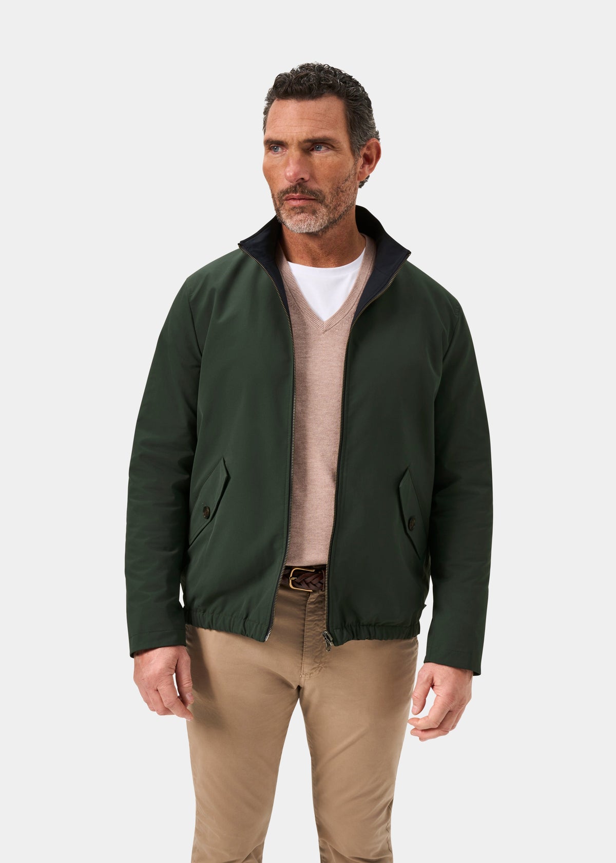 Man wears a Lakeward Men’s Reversible Bomber Jacket in green and navy over a beige sweater with khaki pants.
