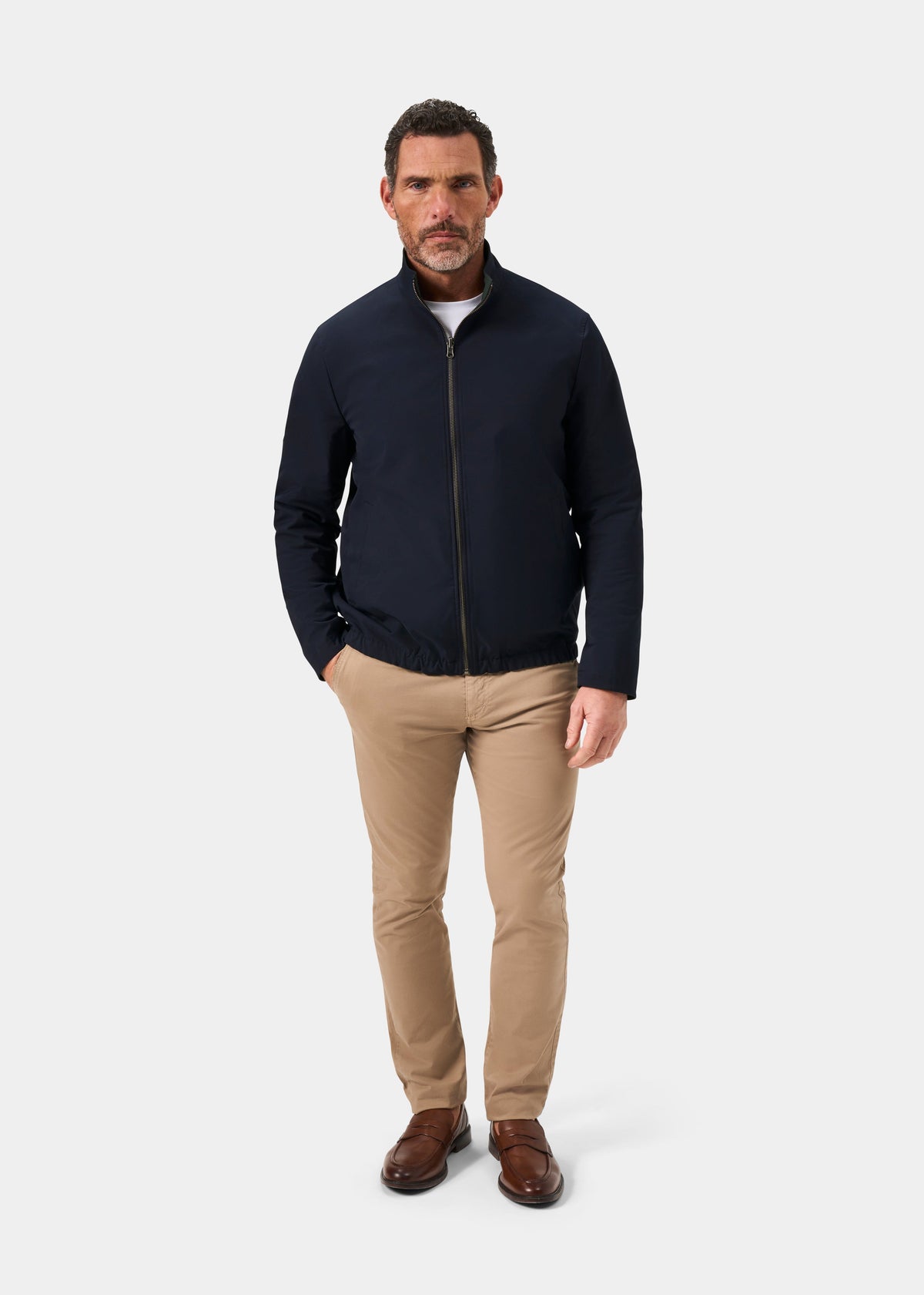 Man wearing Lakeward Men’s Reversible Bomber Jacket in green and navy, beige pants, and brown shoes on a white background.