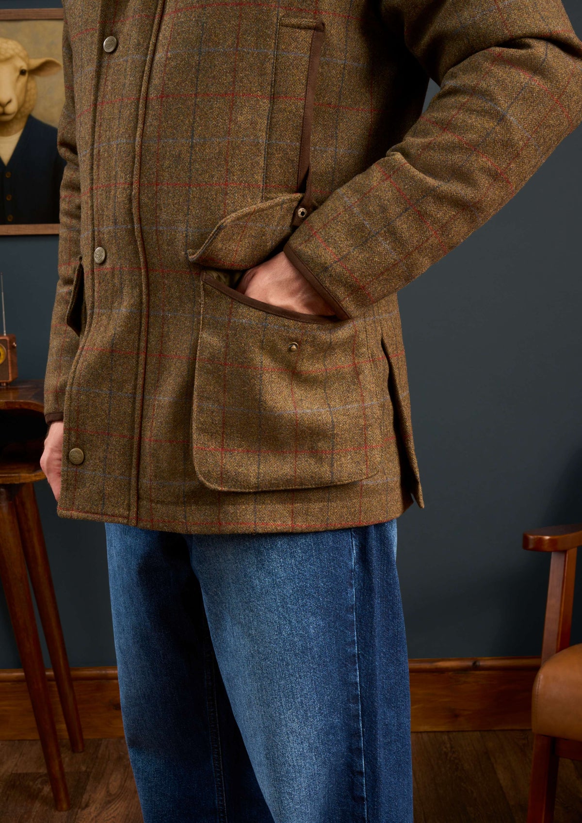 Person in a Surrey Men’s Tweed Waterproof Coat in Hawkswood (Shooting Fit) and blue jeans stands with hand in pocket.
