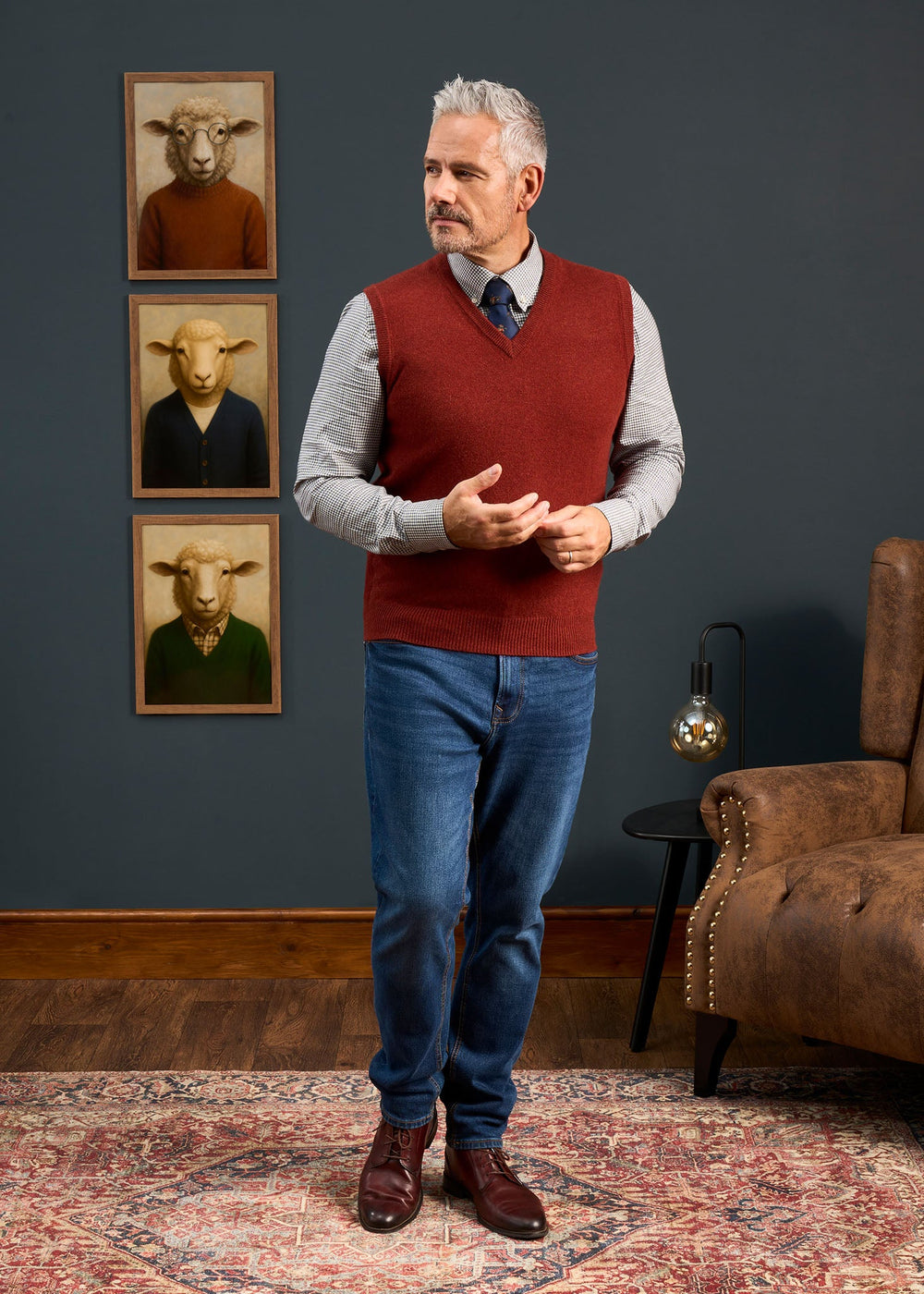 A man in a Norfolk Lambswool V-Neck Slipover In Sienna, worn over a patterned button-down shirt and blue jeans.