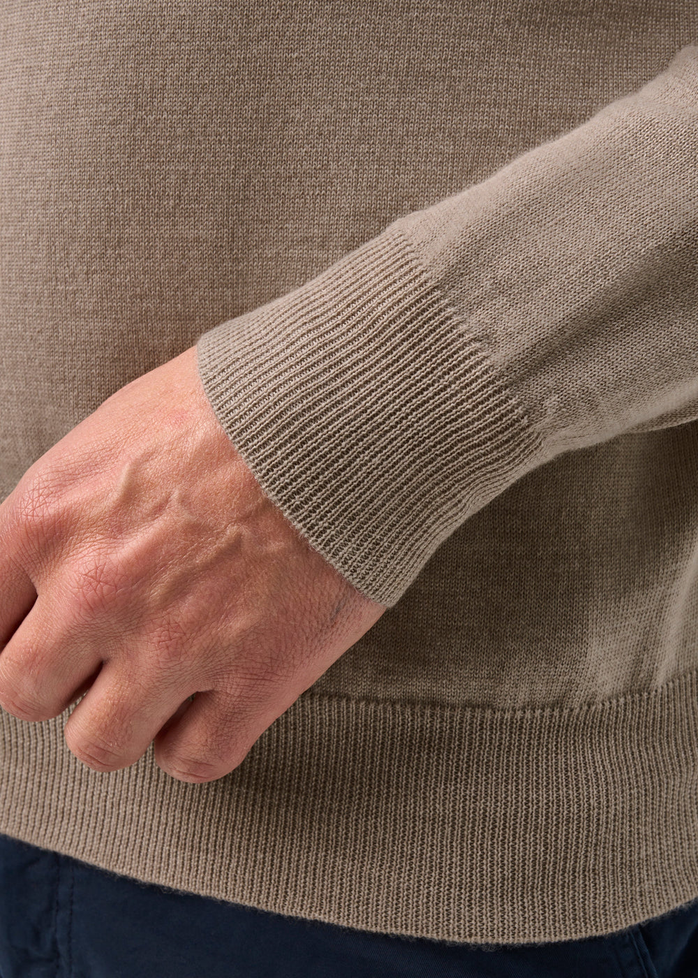 A close-up of a hand in the Barton Merino Wool Quarter Zip Jumper in Cobble, cuff visible, with dark blue pants.