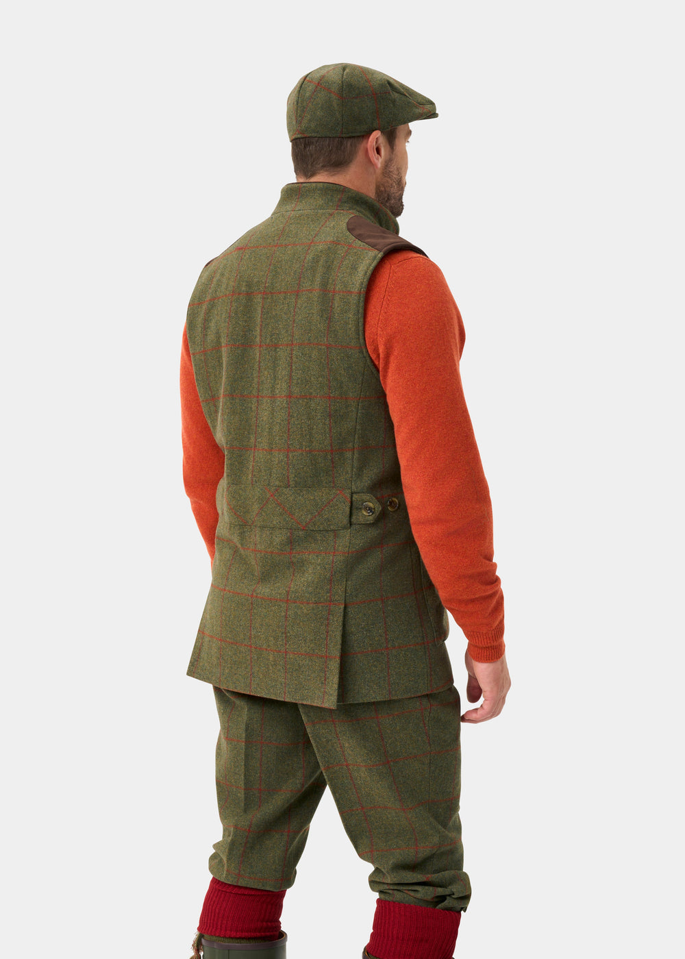 Man in Combrook Men’s Tweed Water Repellent Shooting Gilet in Reed, matching pants, orange sweater, cap, red socks.