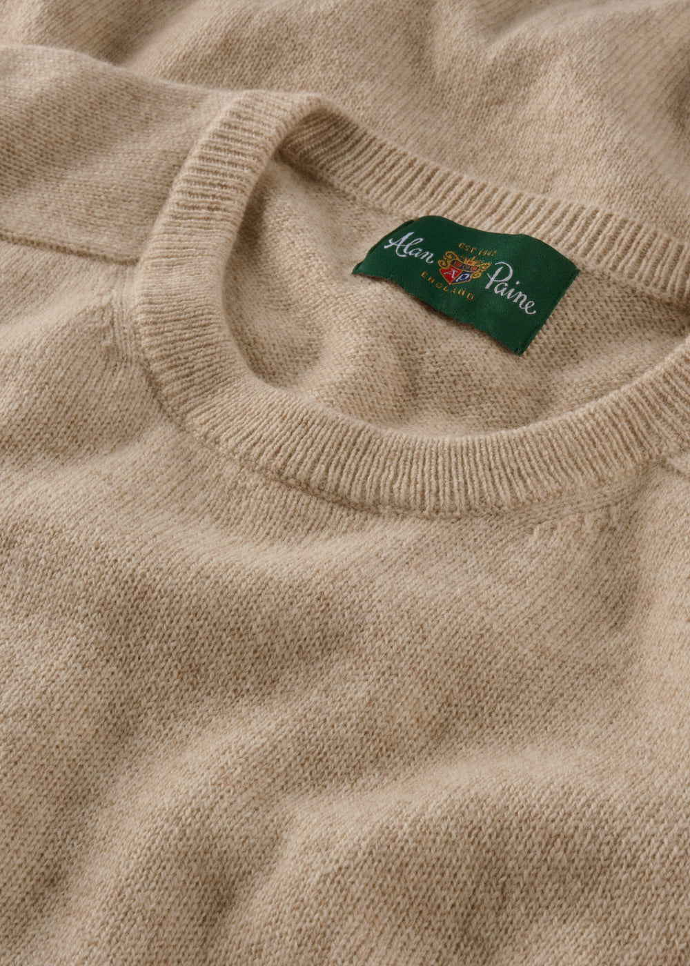 Close-up of a beige sweater with a brand label on the collar.